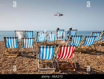 Zwei Personen sitzen auf Liegestühlen am Strand von Brighton beobachten Air Sea Rescue Helicopter Stockfoto