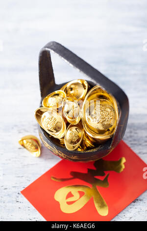 Das chinesische Neujahr - Gold sycee (fremden Text bedeutet Wohlstand) und roten Paket (ausländische Text bedeutet Frühling Saison) auf weiß lackiertes Holz Tisch Stockfoto