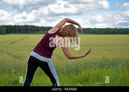 Frau mittleren Alters Yoga Stretching und Bewegung im Freien. Rückansicht, Feld für den Hintergrund. Stockfoto