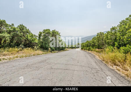 Zurück Straße mit Rissen in den Bürgersteig und keine Linien zu teilen, um es zu einem Neblig oder dunstig Tal führenden Stockfoto