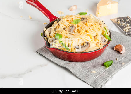 Cremige Pilze Pasta mit Käse und Basilikum, portioniert in der Pfanne, auf weissem Marmortisch, kopieren Raum Stockfoto