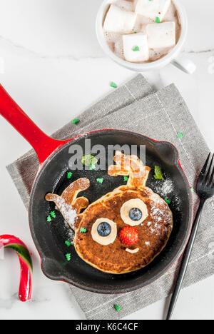 Lustig Essen für Weihnachten. Kinder Frühstück Pfannkuchen wie Rentier dekoriert, mit heißer Schokolade mit Marshmallows, weiße Tabelle kopieren Raum, Ansicht von oben Stockfoto