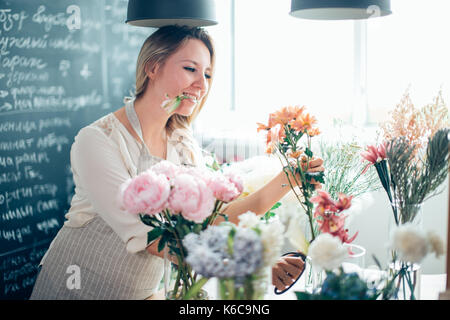 Schöne junge Frau Floristen arrangieren Pflanzen im Blumenladen lächelnd Stockfoto