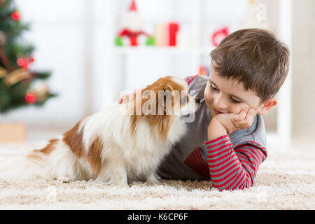 Little Baby Junge mit Hund liegend auf dem Boden Weihnachtsbaum Stockfoto