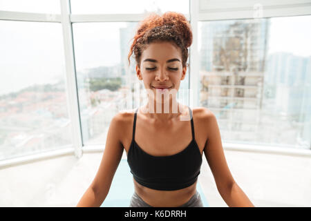 Junge afrikanische Frau mit lockigem Haar in Sportkleidung, Yoga Übung auf dem Boden zu Hause Stockfoto