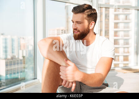 Lächelnd bärtigen Mann in der Nähe der Fenster zu Hause sitzen Stockfoto
