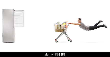 Kerl mit einem Einkaufswagen voller Lebensmittel gegen einen leeren Kühlschrank auf weißem Hintergrund gezogen Stockfoto