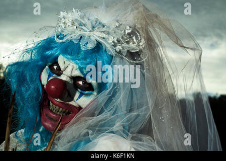 Nahaufnahme der Ein unheimlich bösen Clown tragen eine schmutzige und ausgefranster Braut Kleid, in einem beunruhigenden Landschaft bei Nacht Stockfoto