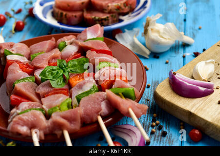 Nahaufnahme von einigen raw-Türkei Fleischspieße mit Gemüse in einem Steingut Teller gemischt, auf einem blauen Holzmöbeln im Landhausstil Tisch Stockfoto