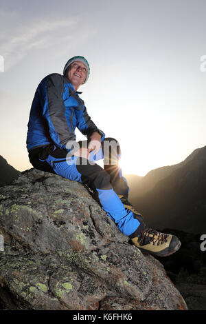 Gut aussehende junge Wanderer eine Pause auf einem Stein und genießt den Sonnenaufgang in den Schweizer Bergen Stockfoto