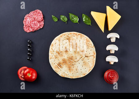 Rohe Pizza Teig mit Zutaten zum Kochen vegetarische Pizza auf dem dunklen Stein Oberfläche mit Rand, Ansicht von oben. Stockfoto