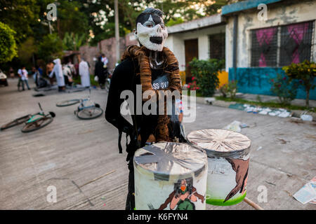 Eine junge Salvadorianische Mann, das Tragen einer Maske mit Gesicht Farbe, trägt Drums vor Beginn der La Calabiuza Parade am Tag der Toten feier Ich Stockfoto