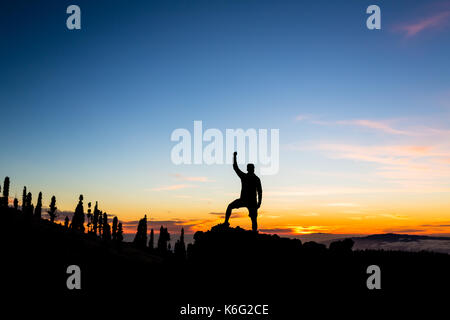 Mann feiern Sonnenuntergang in den Bergen mit ausgestreckten Armen. Trail Runner, Wanderer oder Bergsteiger mit erhobenen Händen erreicht ein Ziel auf einem Berg, enjo Stockfoto