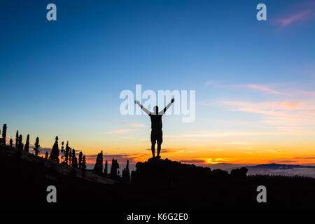 Mann feiern Sonnenuntergang mit ausgestreckten Armen in den Bergen. Trail Runner, Wanderer oder Bergsteiger mit erhobenen Händen oben auf einem Berg erreicht, genießen Sie inspirat Stockfoto