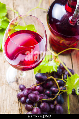 Glas Rotwein mit Trauben auf einem rustikalen Holzmöbeln Hintergrund Stockfoto