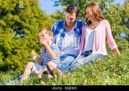Familie sitzt auf der Wiese spielen mit Seifenblasen Stockfoto