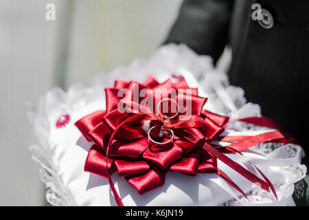 Gold Trauringe auf dem Kissen mit bordeaux Farbband in den Händen der Jungen. Stockfoto