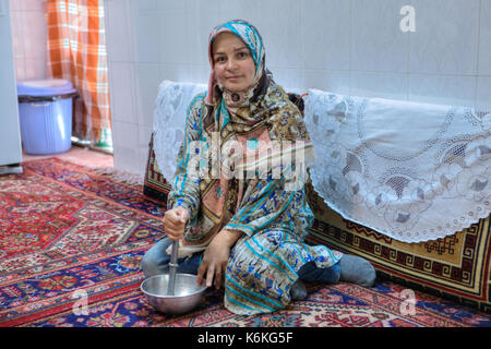 Provinz Fars, Shiraz, Iran - 18. April 2017: muslimische Frau in Tracht Vorbereitung essen, sitzen auf dem Boden zu Hause, sie schleift Produkte mit einem Stockfoto