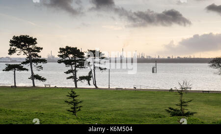 Den Sonnenuntergang Silhouetten der industriellen Türme von Esso Fawley Ölraffinerie und Bäume im netley Country Park an den Ufern des Southampton Wasser. Stockfoto