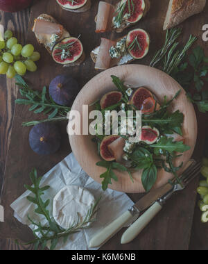 Einfache Diät Salat mit Rucola, Feigen und Blauschimmelkäse auf ein braunes Holz- Oberfläche. Sandwiches mit Ricotta, frische Feigen, Prosciutto, Rosmarin und blauen Käse Stockfoto