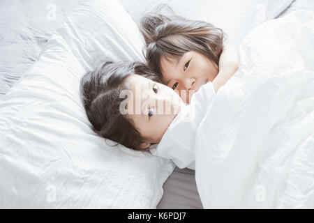 Zwei kleine asiatische chinesische Mädchen Hug zusammen und auf dem Bett liegen. Stockfoto