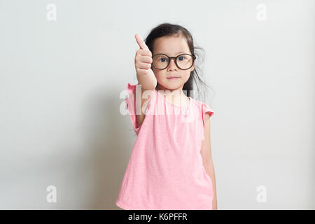 Kleine Mädchen in rosa gekleidet zeigt "Daumen hoch" Geste, auf weißem Hintergrund. Stockfoto