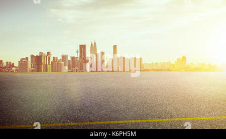 Blick auf den leeren asphaltierte Straße mit Sicht auf die City Skyline im Hintergrund. Sonnenuntergang sonnenaufgang Szene. Stockfoto