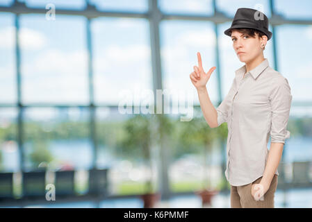 Schwere Mädchen hält Finger Pistole und trägt einen schwarzen Hut im Büro Stockfoto