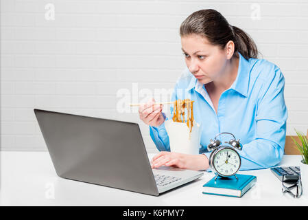 Frau Buchhalter Essen Nudeln zum Mittagessen Pause und Arbeiten am Laptop Stockfoto