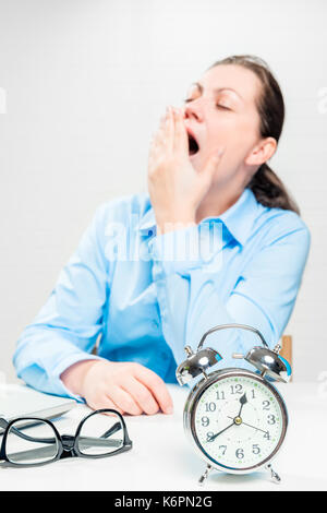 Müde gähnen Frau in einem Büro außerhalb des Fokus und ein Wecker closeup Stockfoto