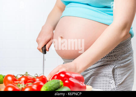Großen Bauch der schwangeren Frau im Fokus, Frau salat Vorbereiten von Gemüse Stockfoto
