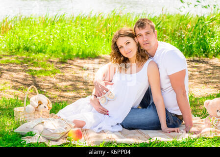 Picknick in der Nähe des Sees, junge schwangere Paare auf einer Plaid Stockfoto