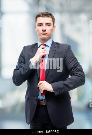 Mann in Anzug korrigiert rote Krawatte, Portrait im Büro Stockfoto