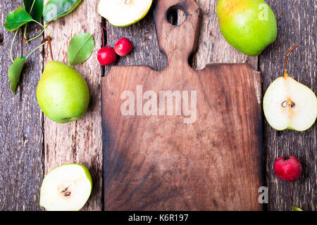 Birne und kleinen Apple um leer Schneidbrett auf Holz rustikale Hintergrund. Ansicht von oben. Rahmen. Herbst Ernte. Platz kopieren Stockfoto