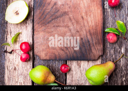 Birne und kleinen Apple um leer Schneidbrett auf Holz rustikale Hintergrund. Ansicht von oben. Rahmen. Herbst Ernte. Platz kopieren Stockfoto