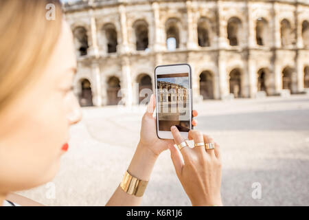 Junge Frau Touristen fotografieren mit Smartphone antiken Amphitheater in der Altstadt von Nimes während der sonnigen Morgen in Frankreich Stockfoto