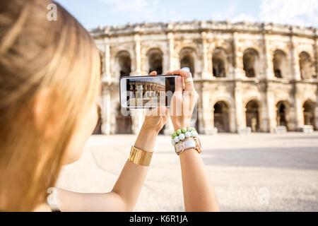 Junge Frau Touristen fotografieren mit Smartphone antiken Amphitheater in der Altstadt von Nimes während der sonnigen Morgen in Frankreich Stockfoto
