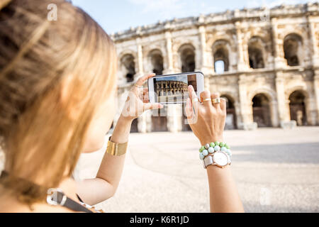 Junge Frau Touristen fotografieren mit Smartphone antiken Amphitheater in der Altstadt von Nimes während der sonnigen Morgen in Frankreich Stockfoto