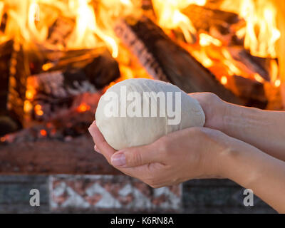 Frau Hände, frischen, rohen Teig für Pizza oder Brot backen auf holztisch vor dem brennenden Kamin. Komfort Stimmung Konzept Stockfoto