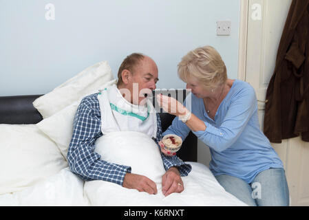 Eine ältere kranke bettlägerigen Mann Frühstück gespeist durch seine Frau und seine Helfer, Stockfoto