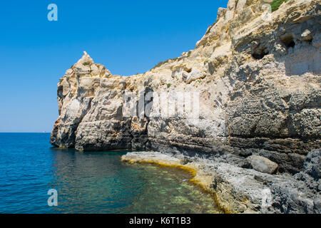 Eine Felswand entlang der maltesischen Küste, die Funktionen von Meer Erosion und Cliff Rezession. Wellenschnitt Plattform auf Meereshöhe und Risse und Felsbrocken. Stockfoto
