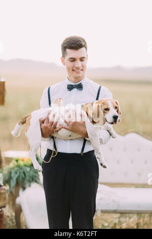 Die Nahaufnahme Porträt des Vintage gekleidet Bräutigam Holding das kleine Flauschige in Punkte Hund im sonnigen Bereich. Stockfoto