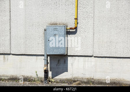 Alte wasser Metallrohre mit Halterungen vor einem Putz an der Wand mit Metall Box für Wasserzähler festgesetzt. Stockfoto