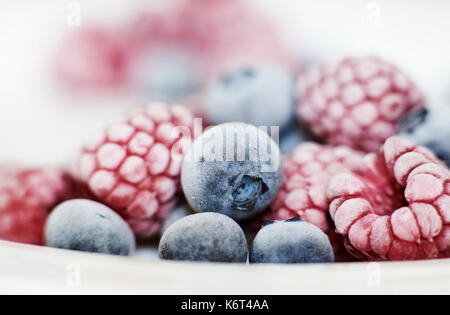 In der Nähe des gefrorenen Heidelbeeren und Himbeeren in einer weißen Schüssel mit Frost auf der Haut mit Vitamin C super Obst zum Frühstück. Stockfoto