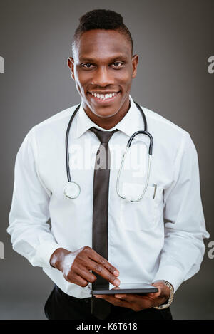 Afrikanische lächelnd Arzt mit Stethoskop stehend und mit digitalen Tablet. Mit Blick auf die Kamera. Stockfoto