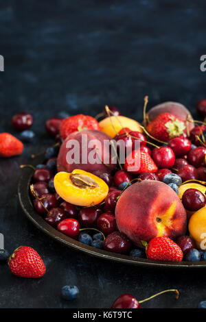 Frische reife Sommerbeeren und Früchte (Pfirsiche, Aprikosen, Kirschen und Erdbeeren) auf Tablett Stockfoto