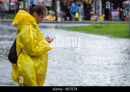 Sarbinowo, Polen - August 2017: Mädchen Kleider im gelben Regenmantel um Hilfe ruft auf Ihrem Mobiltelefon nach extrem starke Regenfälle Stockfoto