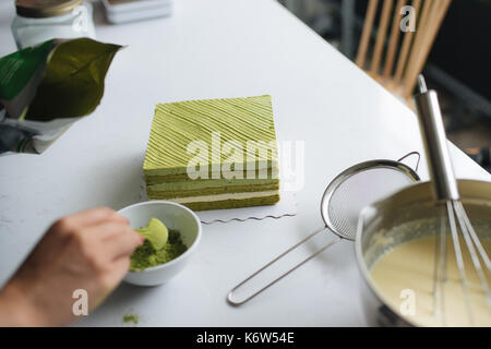 Gießen grüner Tee Pulver über leckeren Käsekuchen Stockfoto