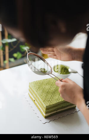 Gießen grüner Tee Pulver über leckeren Käsekuchen Stockfoto