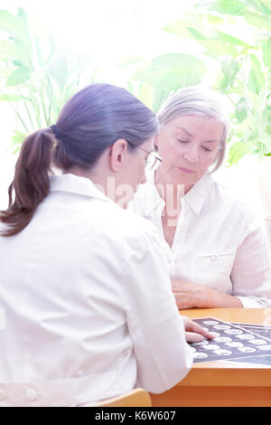 Frauen im mittleren Alter Arzt zeigt Ihr älterer Patienten eine cat-Scan von Kopf, sonnige, helle Atmosphäre Stockfoto